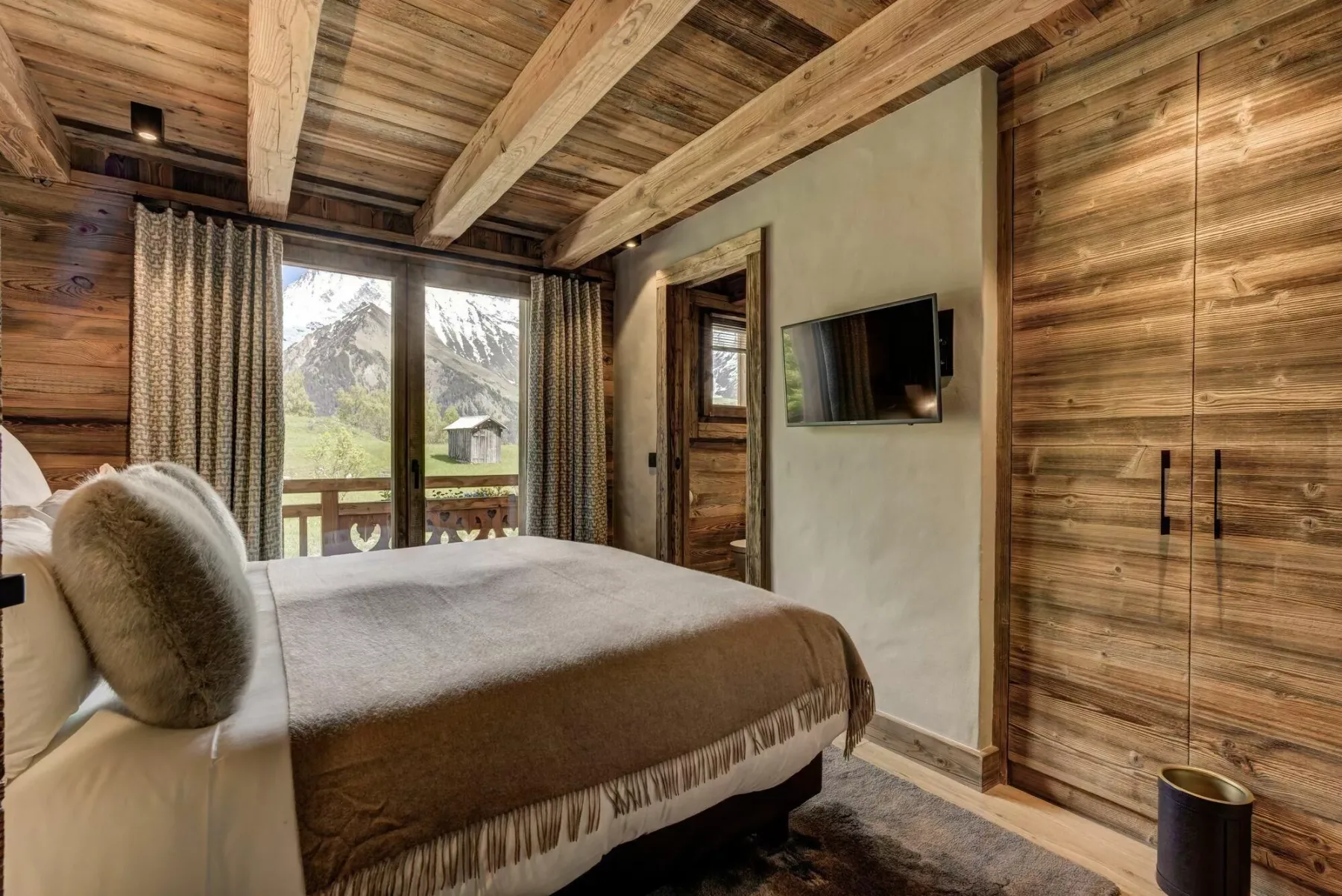 Un dormitorio con una cama, paredes revestidas de madera y una gran ventana con vista a las montañas.