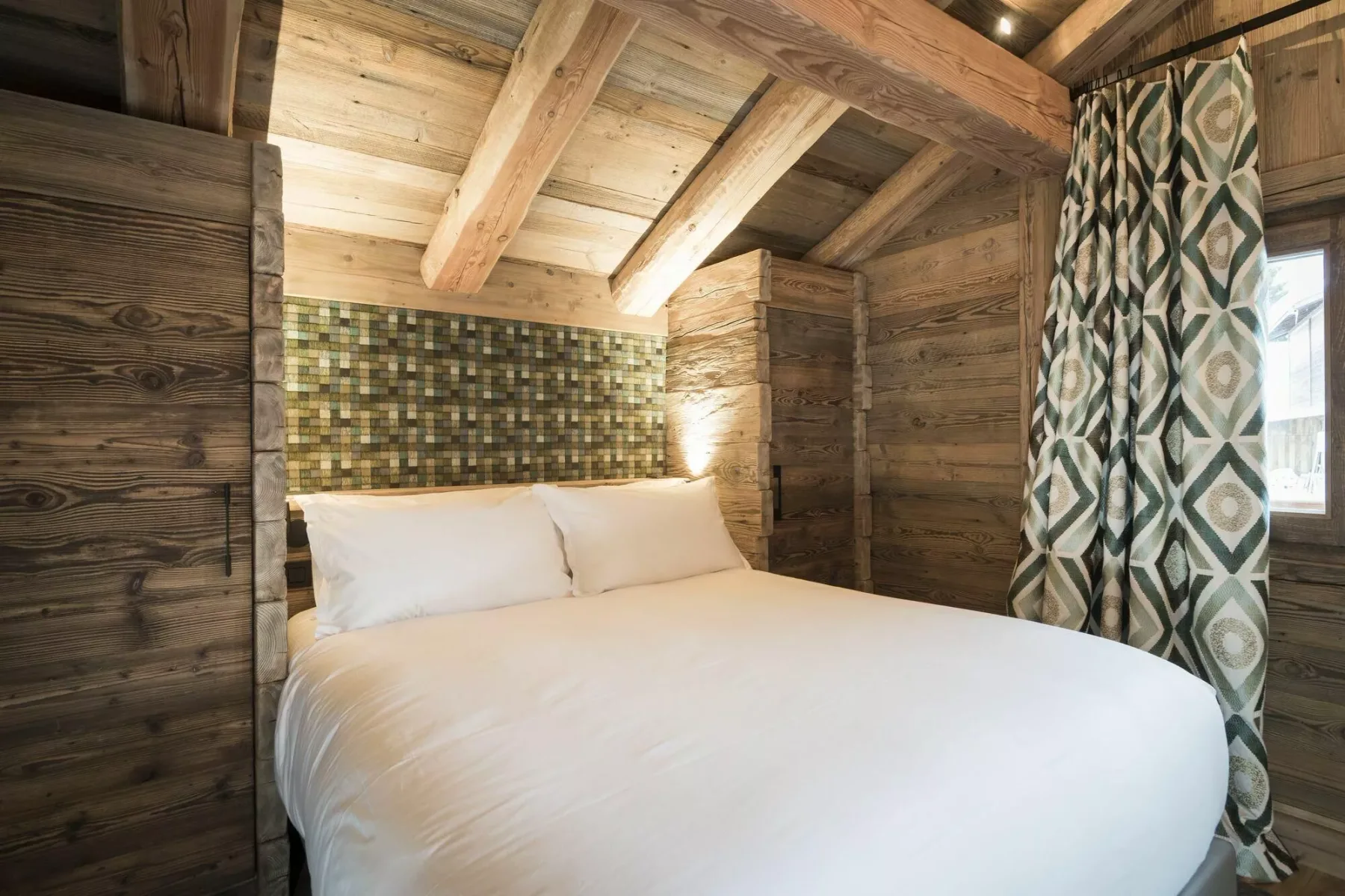 Un dormitorio con una cama blanca bajo vigas de madera expuestas.