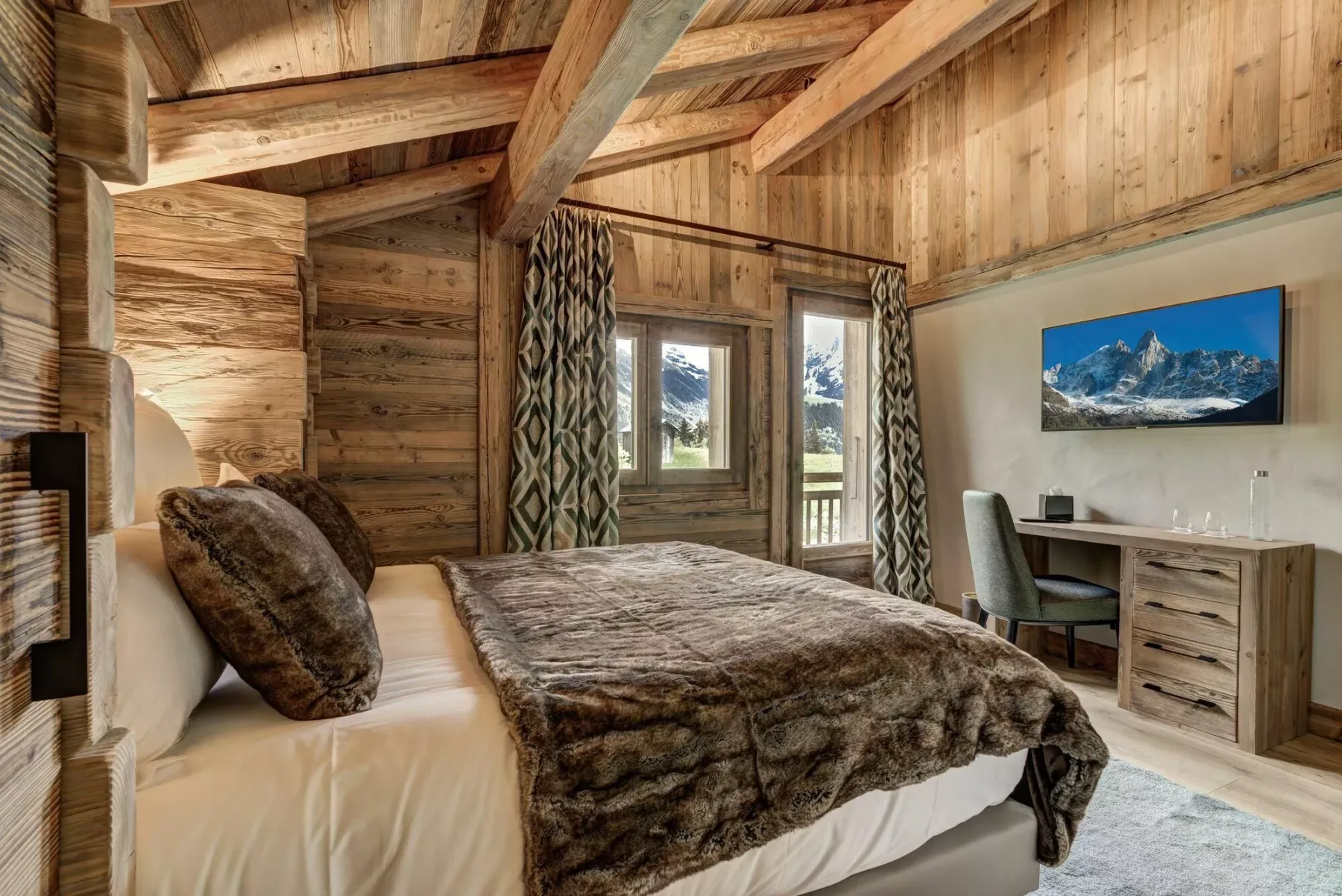 Un dormitorio rústico con cama, paredes revestidas de madera y un escritorio junto a la ventana.