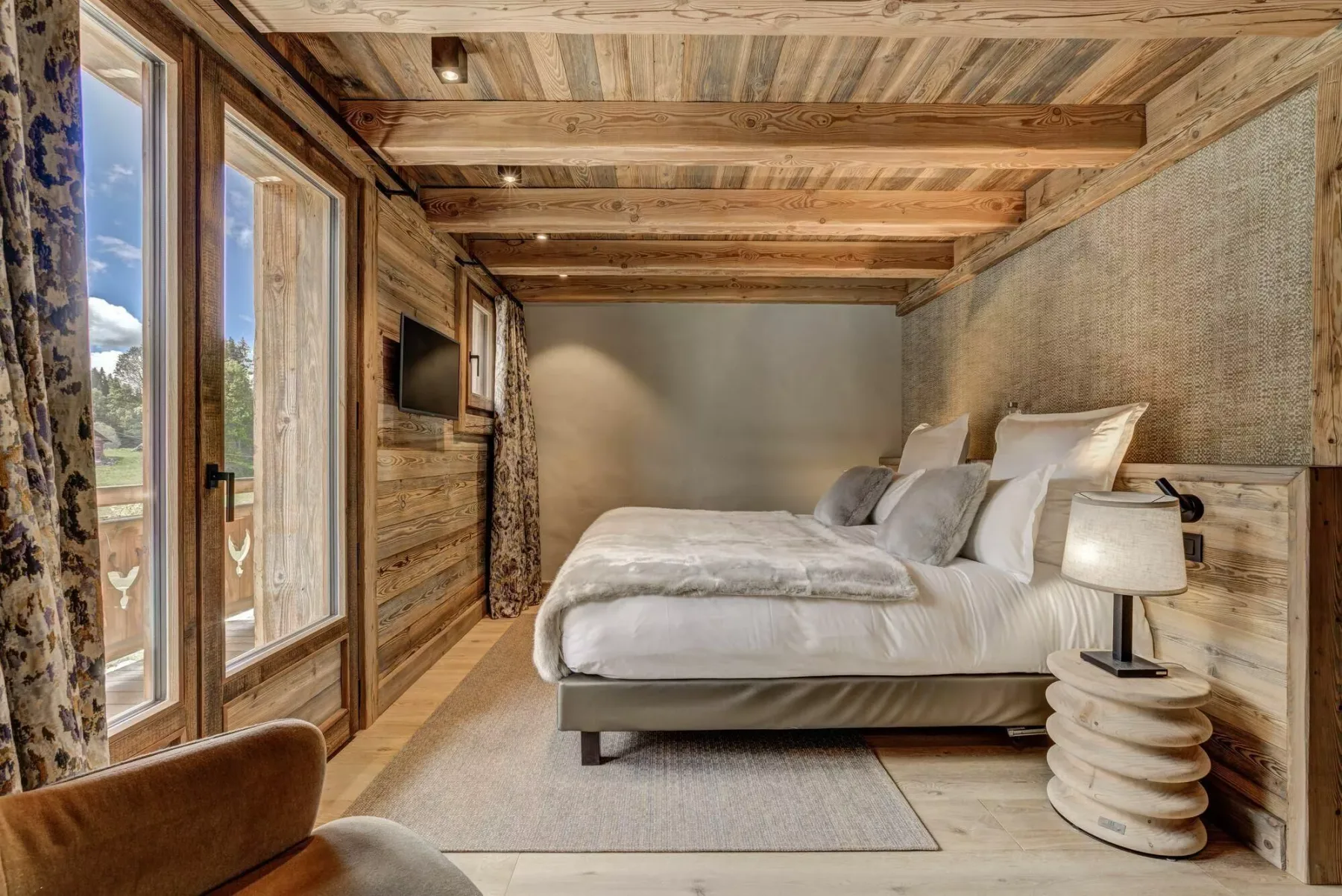 Un dormitorio con una cama grande, vigas de madera en el techo y puertas de vidrio con vistas.