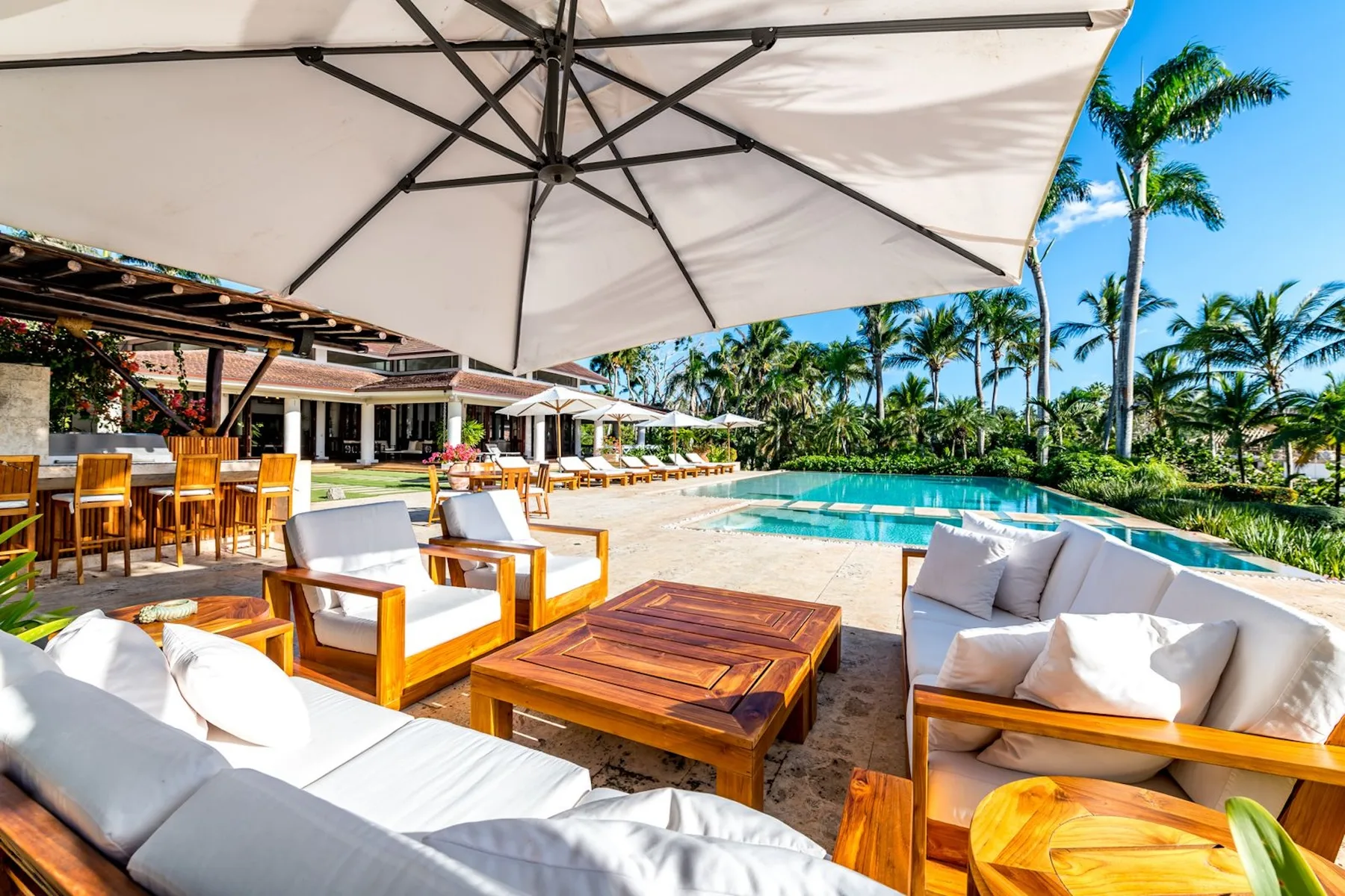 An outdoor poolside lounge with cushioned seating beneath a large umbrella.