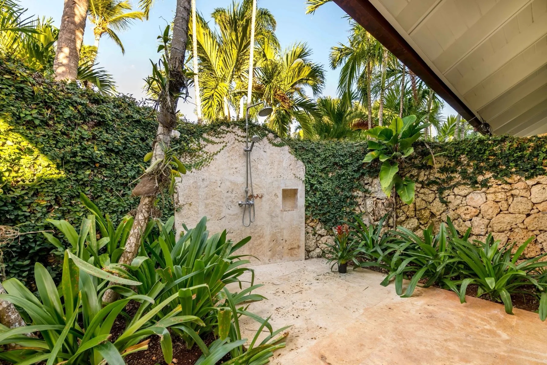 An outdoor shower area surrounded by tropical plants and stone walls.