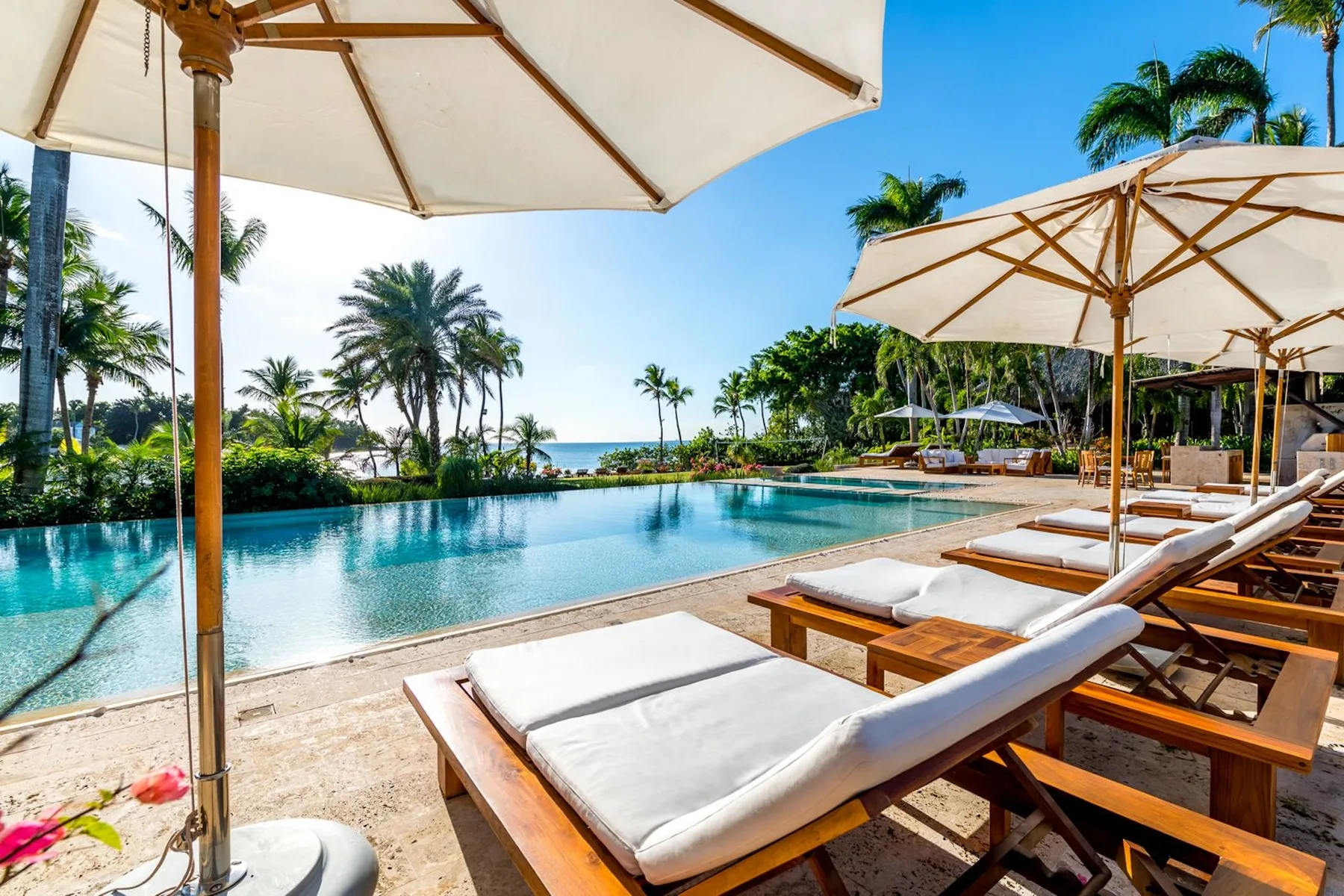 An outdoor pool beside cushioned loungers and large sun umbrellas.