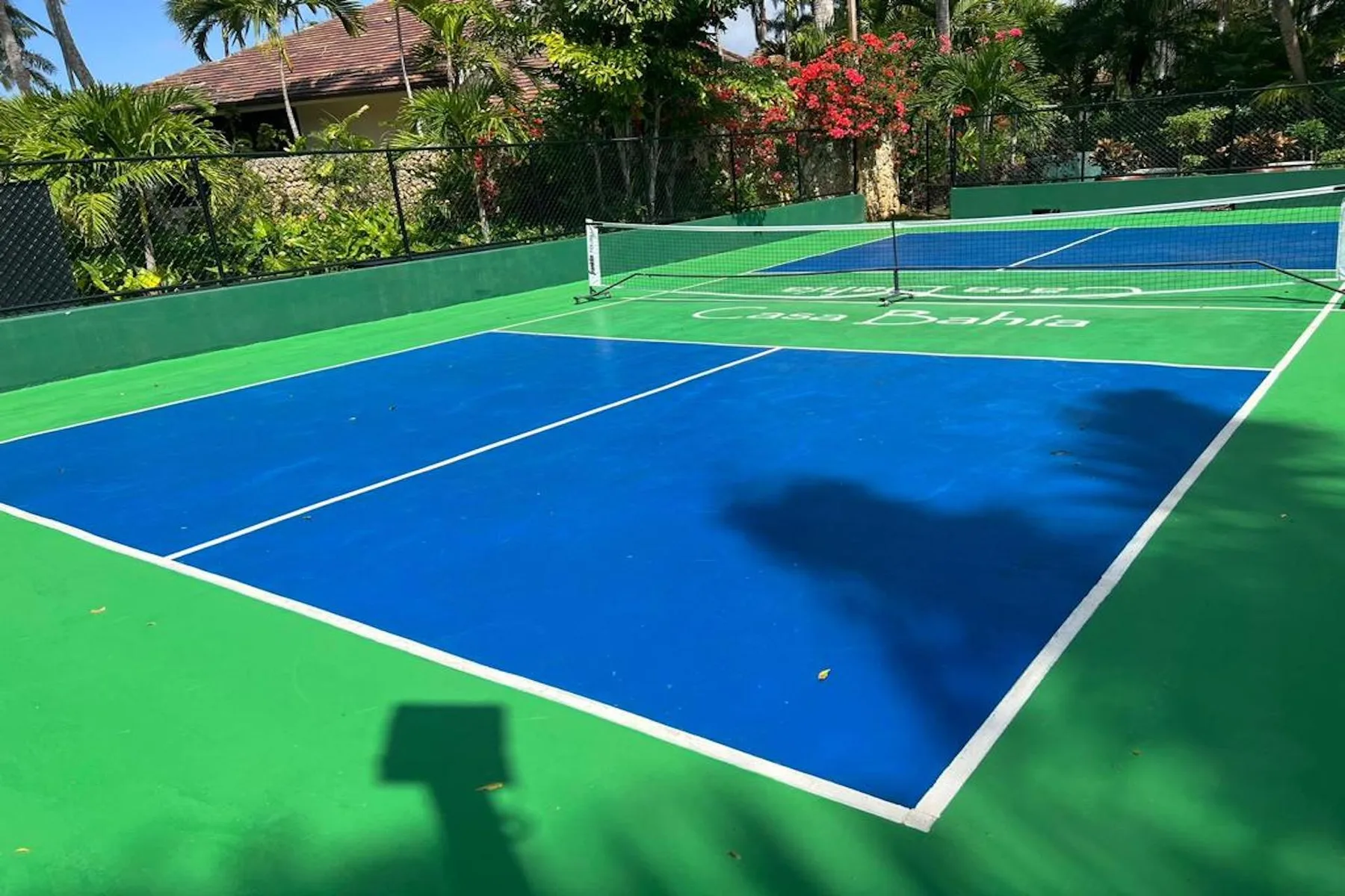 An outdoor tennis court with blue playing surfaces and green borders.