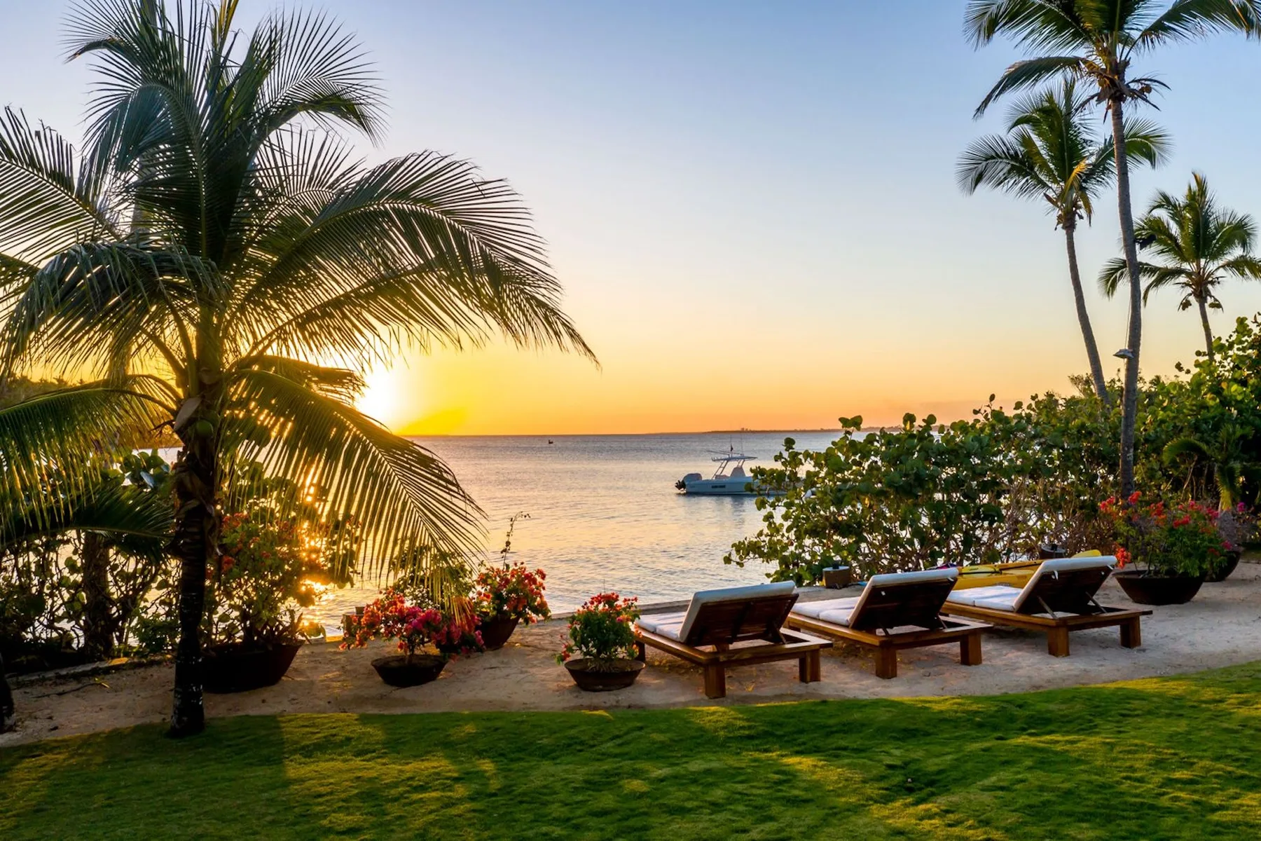 A waterfront patio with lounge seating overlooks the sea at sunset.