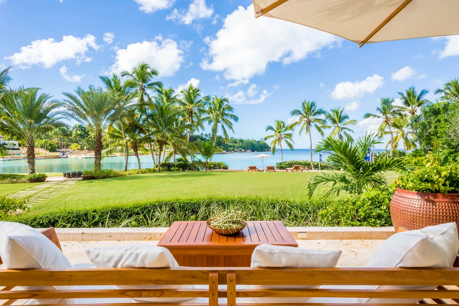 A patio seating area overlooks a palm-lined lawn and blue water.