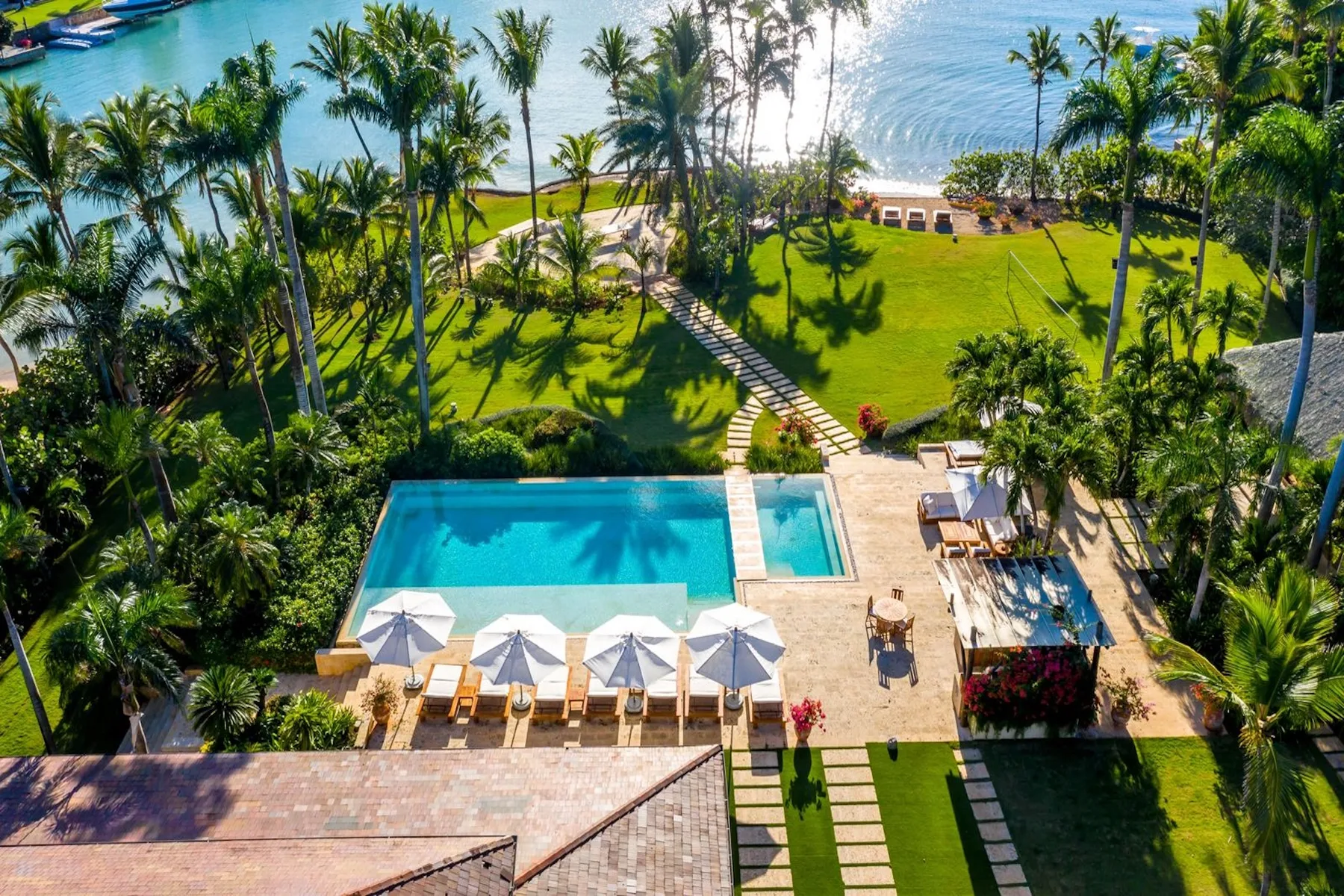 Aerial view of an outdoor pool beside a palm-lined lawn and the water.