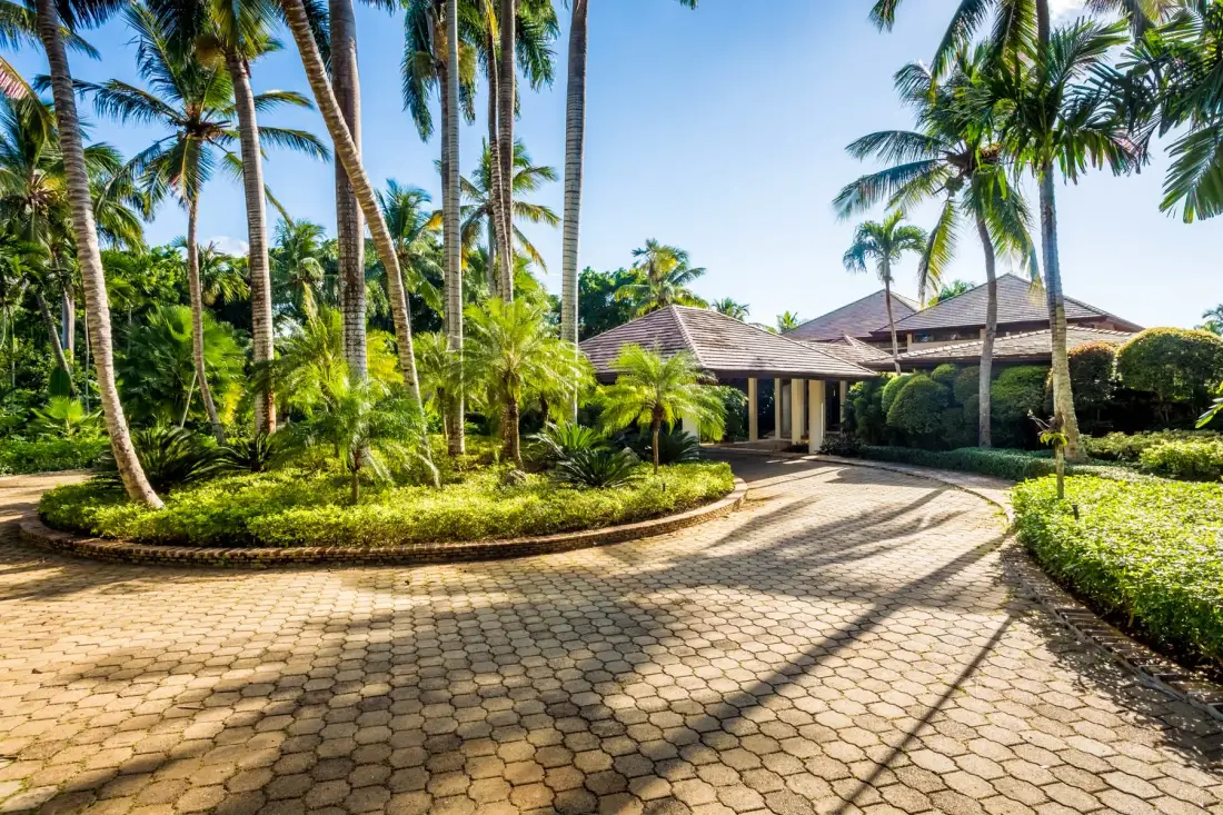 A paved driveway curves through tropical landscaping toward a low building.