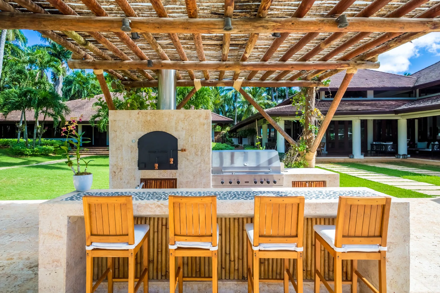An outdoor bar beneath a wooden pergola overlooks a green courtyard.