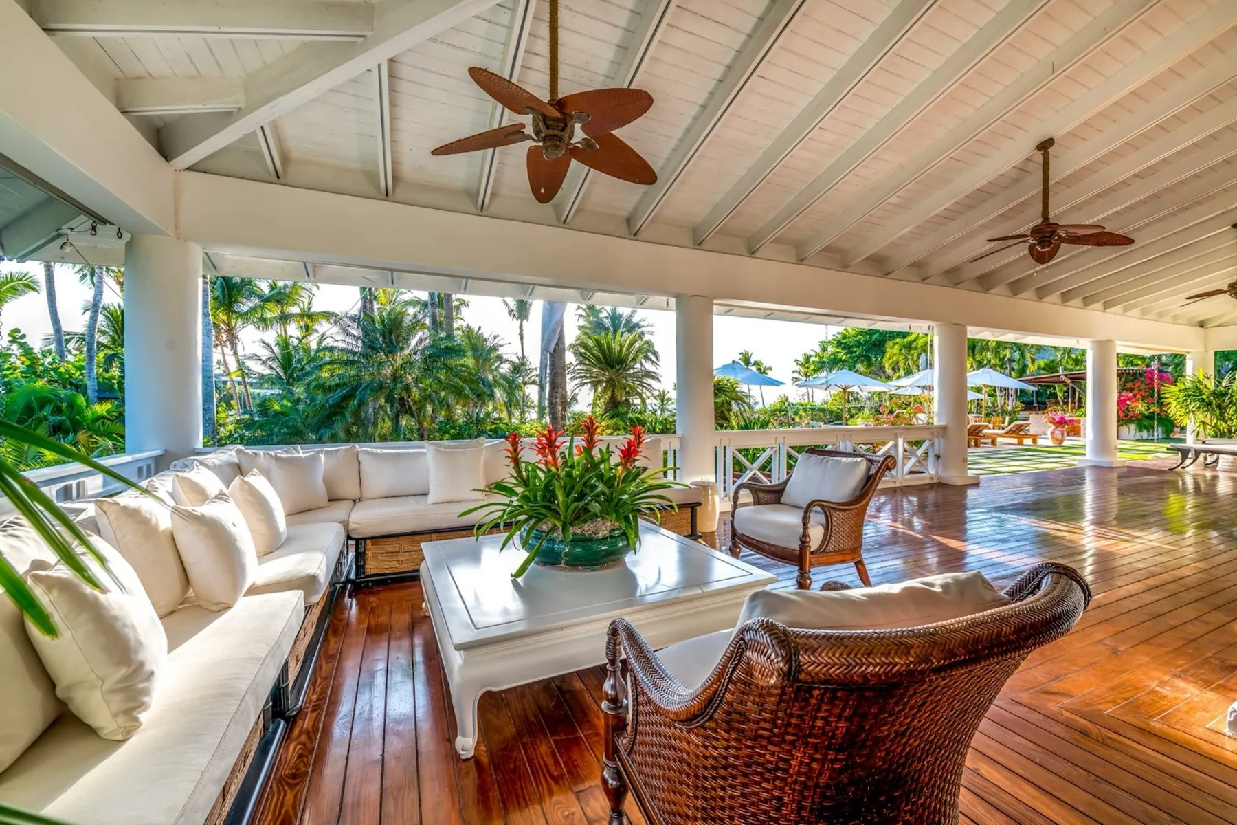 A covered open-air lounge with cushioned seating, wicker chairs, and tropical plants.