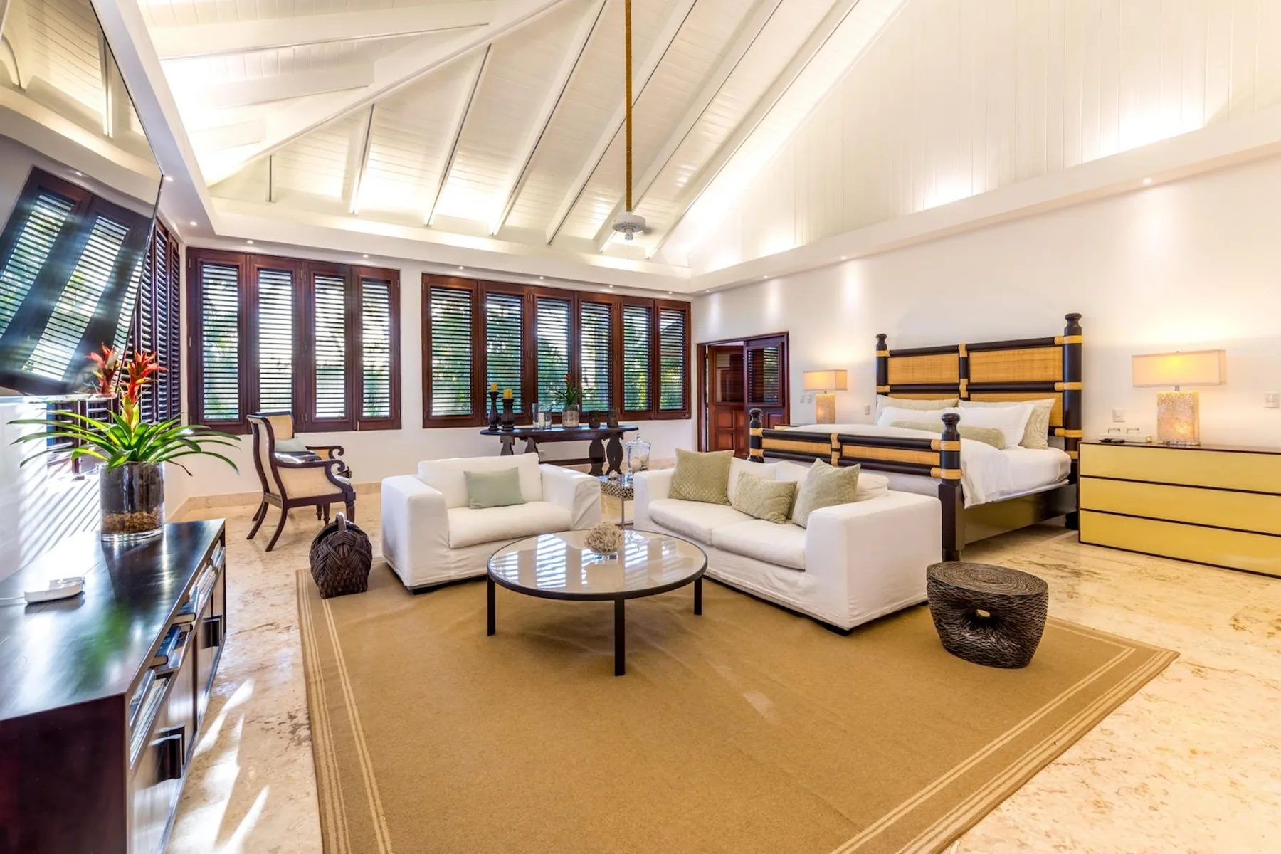 A spacious bedroom with a seating area, large windows, and a king bed.