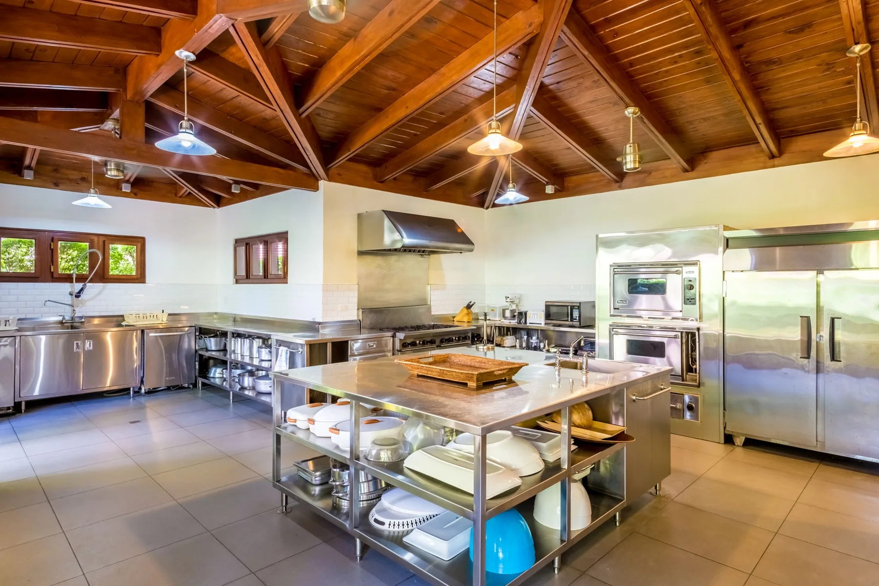 A commercial kitchen with stainless steel worktables beneath a wooden ceiling.
