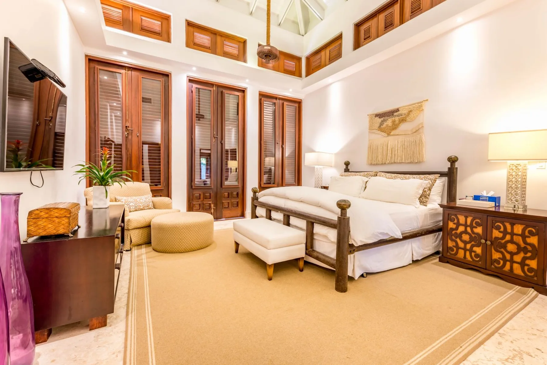 A bright bedroom with a large bed, tall windows, and a seating area.
