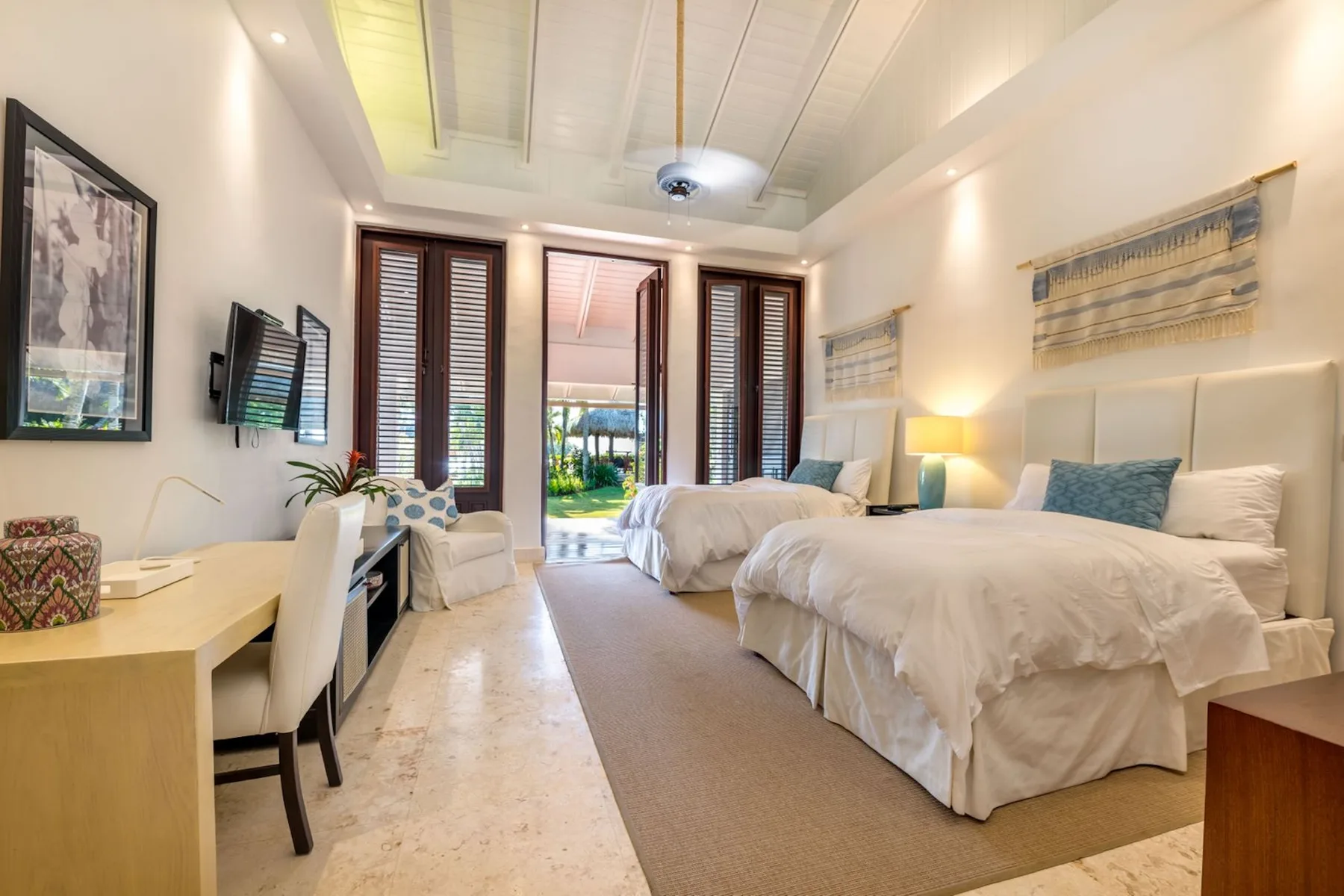 A bright bedroom with two beds and tall shuttered windows.