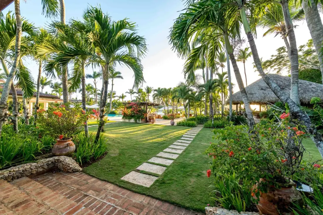 A tropical garden path winds between palm trees and flowering plants.