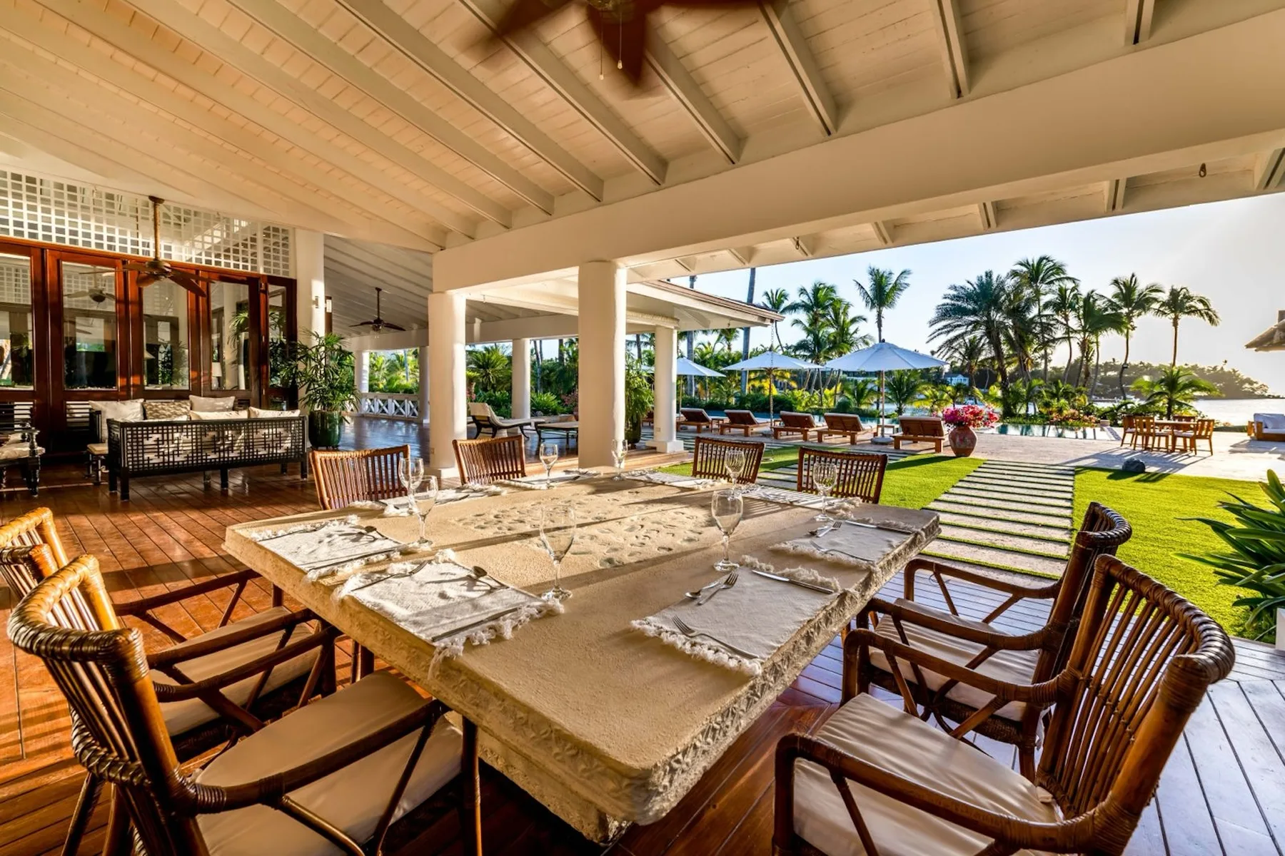 A covered outdoor dining area opens onto a garden with palm trees and a pool.