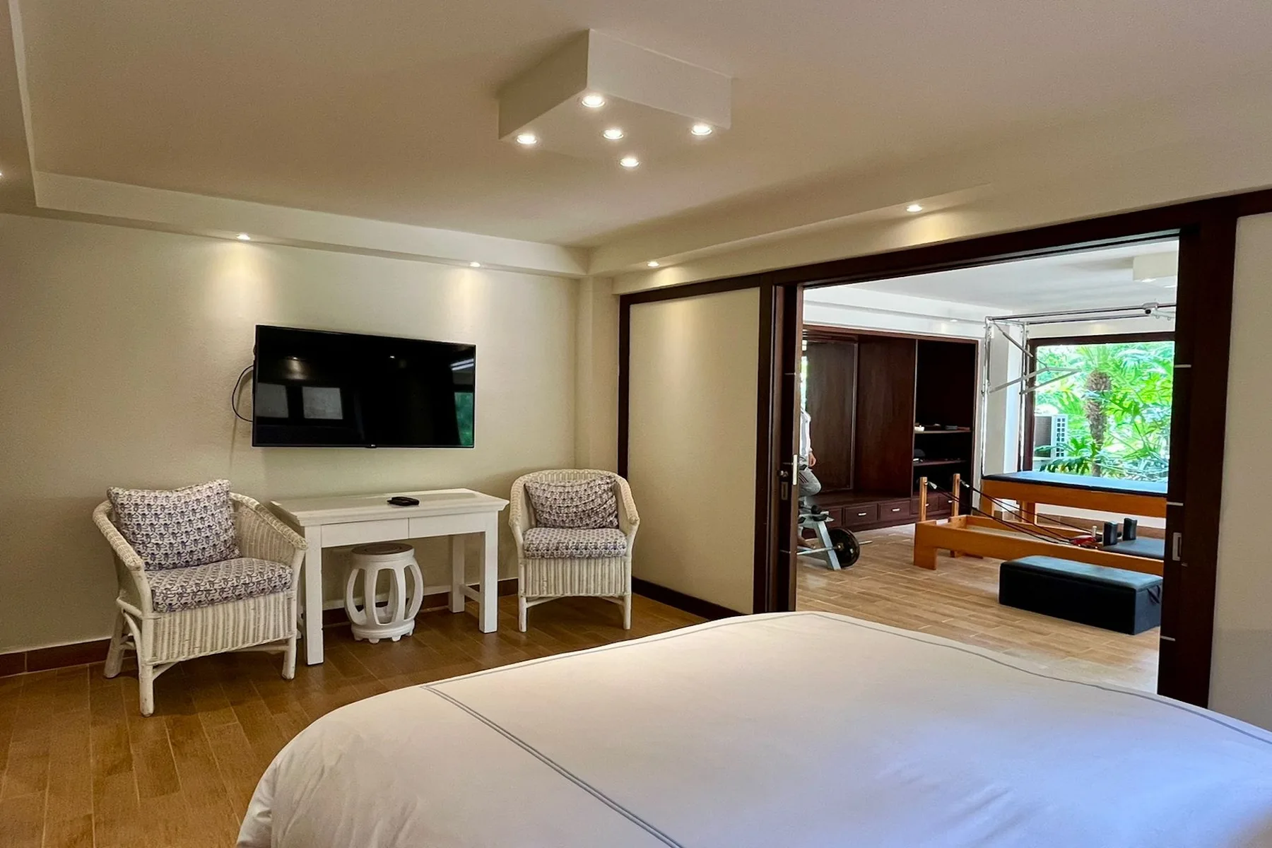 A bedroom with a wall-mounted television and a wide opening to a sitting area.