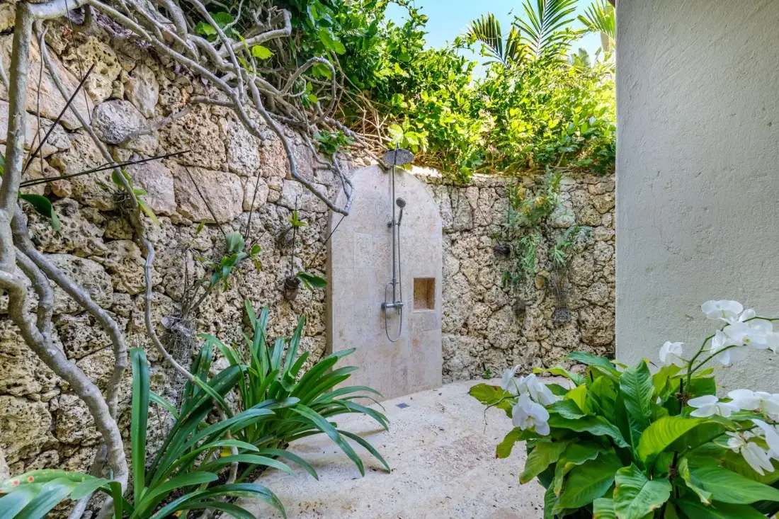 An outdoor shower set among stone walls and tropical greenery.