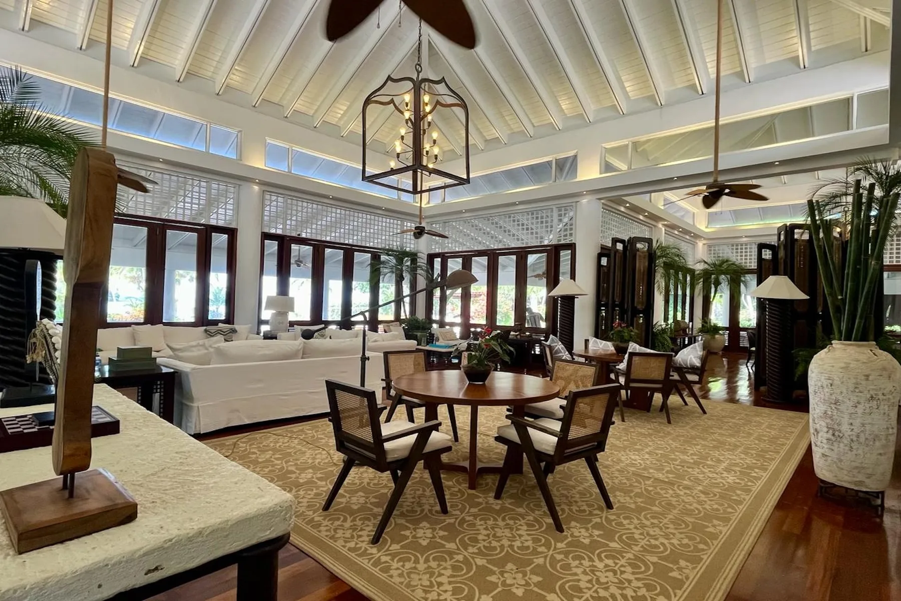 A spacious living room with seating around a dining table beneath a high beamed ceiling.