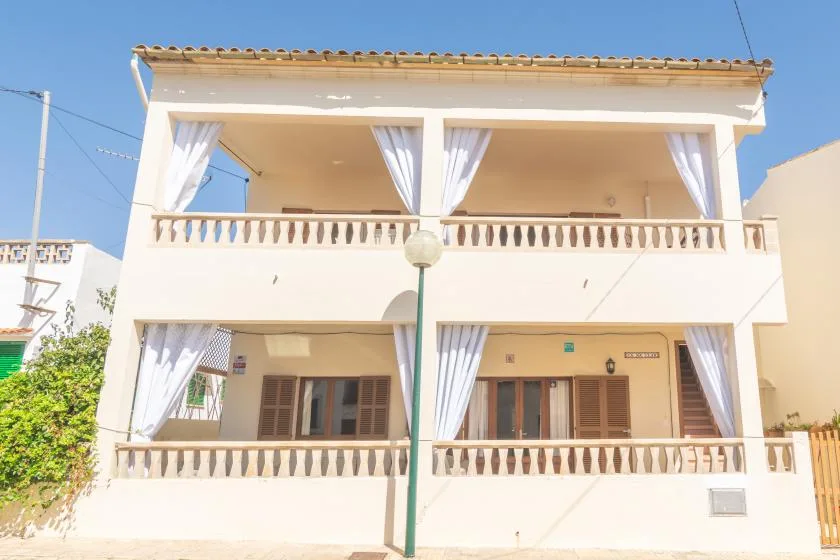 A two-story building has balconies with railings and curtains.
