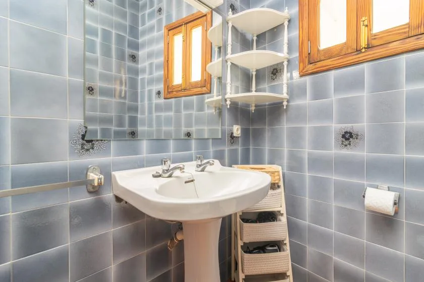 A tiled bathroom with a sink, mirror, and wooden-framed windows.