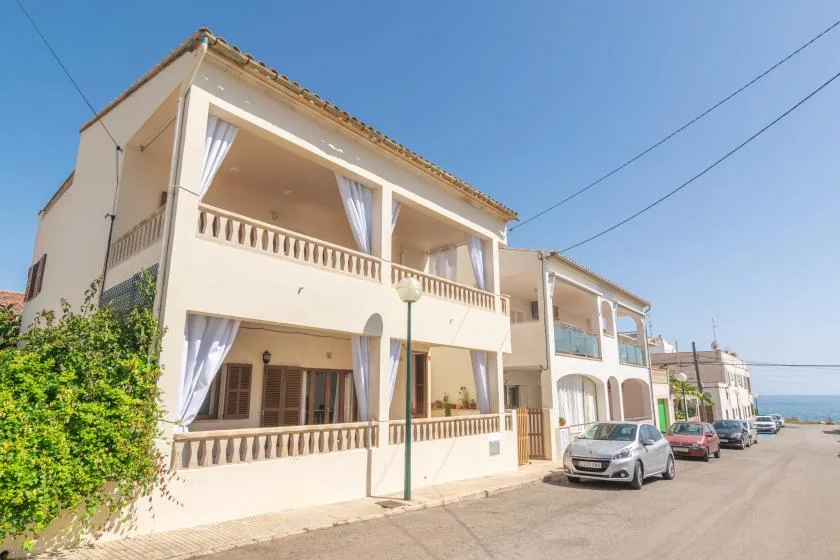 A pale seaside building with open balconies stands beside a coastal street.