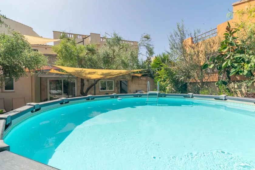 An outdoor swimming pool sits beside a shaded patio and surrounding greenery.