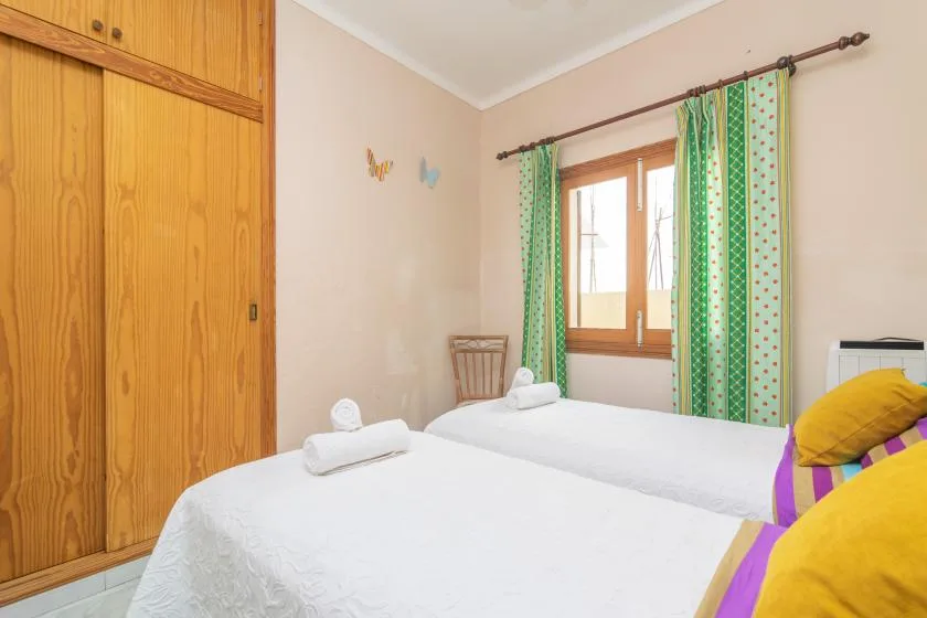 A bedroom with two beds, green curtains, and a wooden wardrobe.