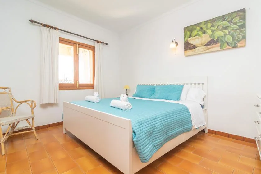 A bright bedroom with a turquoise-covered bed and a window with curtains.