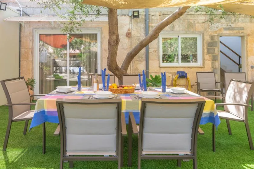 An outdoor dining area with a long table set beneath a shade canopy.
