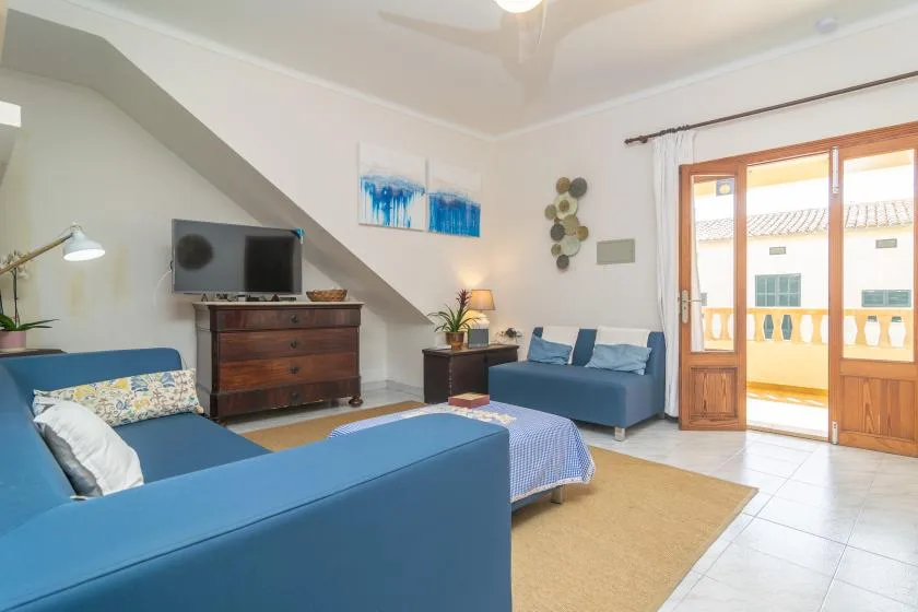 A living room with blue seating, a television, and glass doors opening onto a balcony.