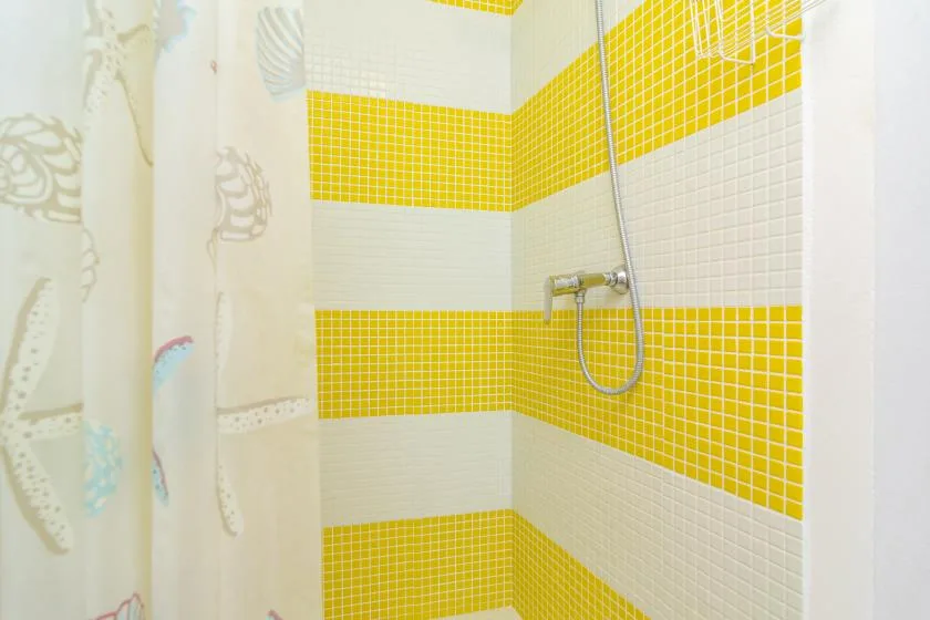 A tiled shower area with bright yellow and white bands beside a patterned curtain.