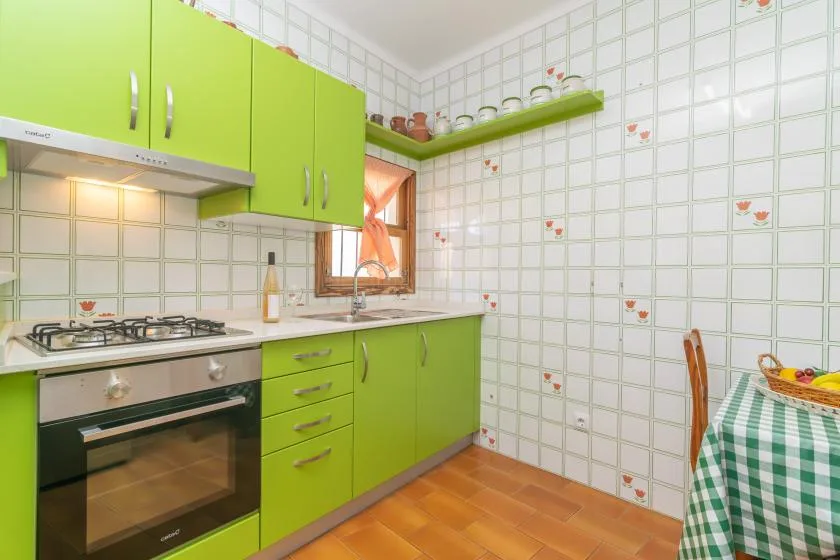 A bright kitchen with green cabinets, a tiled wall, and a checkered tablecloth.