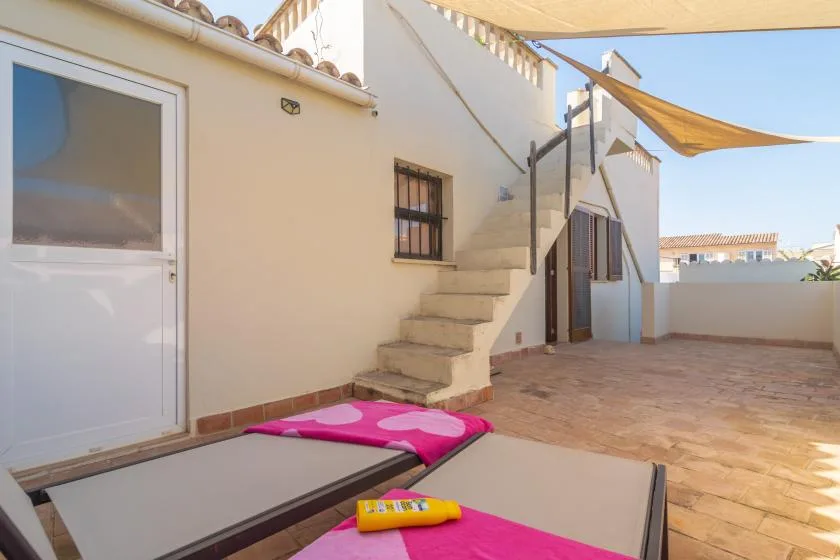 A sunny outdoor terrace with lounge seating, shade sails, and exterior stairs.