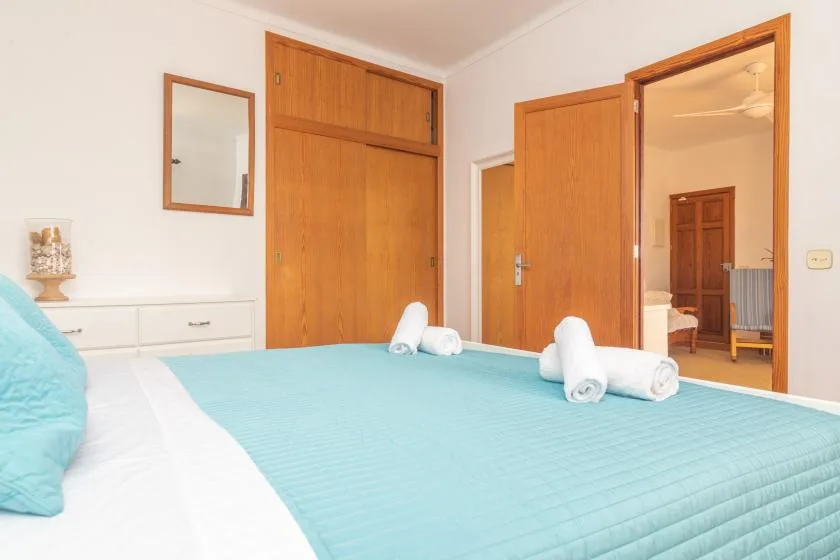 A bedroom with a turquoise bedspread and towels, with an open doorway to another room.