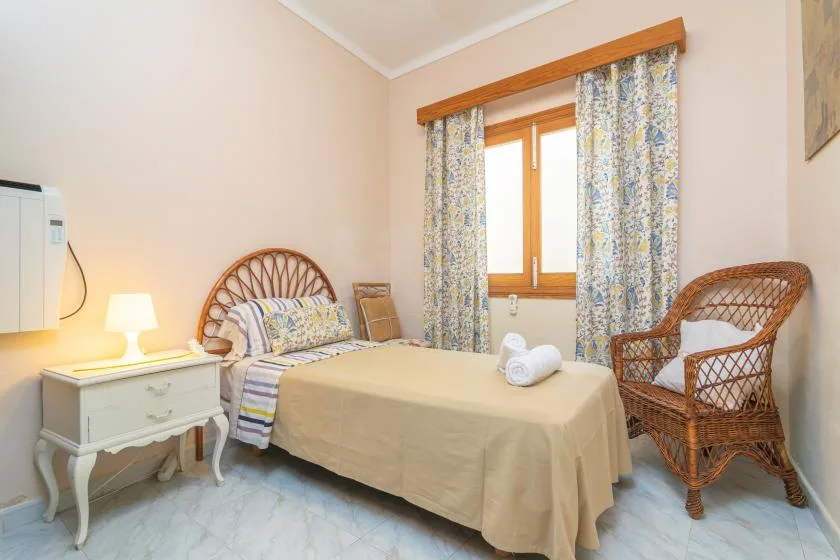 A bedroom with a bed, a window, and a wicker chair.