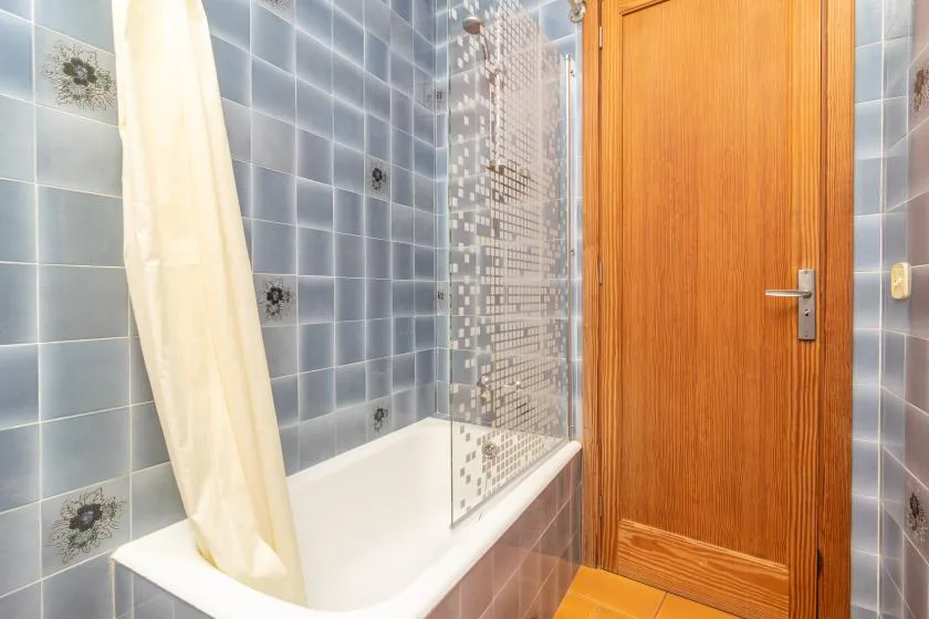 A tiled bathroom with a bathtub and a wooden door.