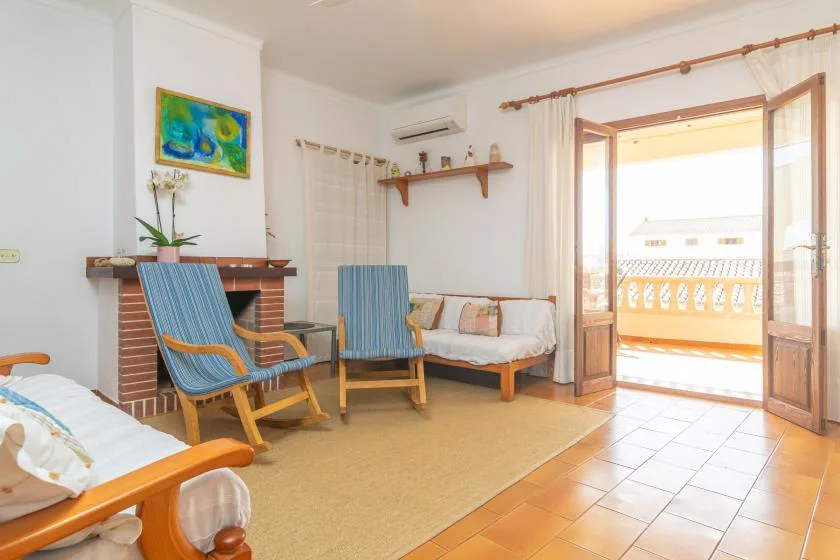 A bright living room with seating, a small daybed, and open doors to a balcony.