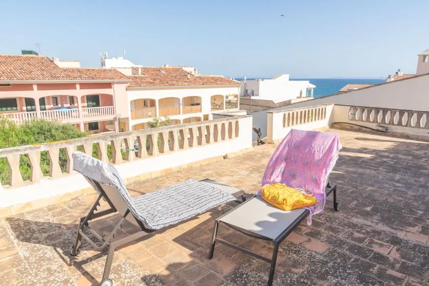 A sunlit rooftop terrace with reclining loungers and a view of the sea.