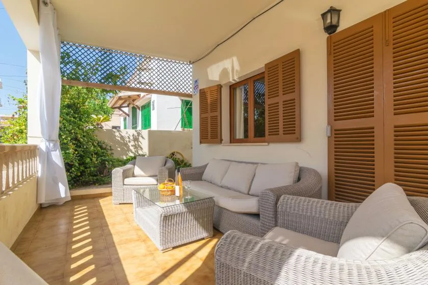 A covered outdoor seating area with wicker furniture and wooden shutters.