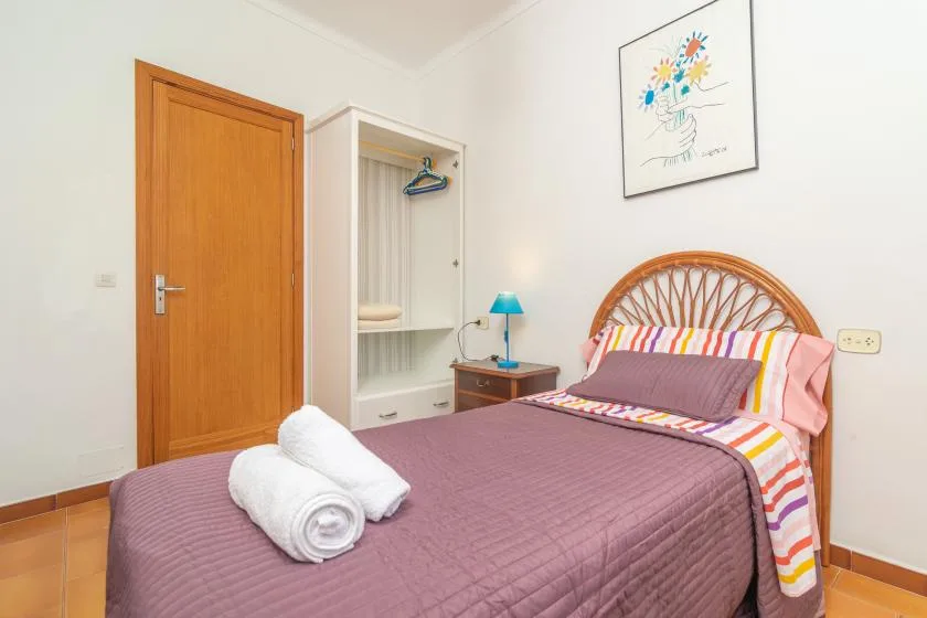 A bedroom with a bed, folded towels, and an open wardrobe.