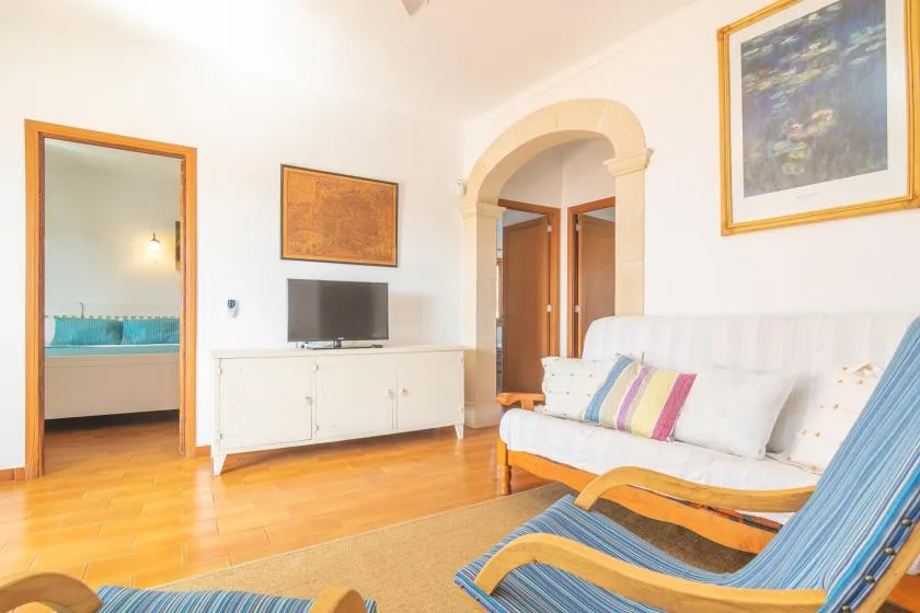 A bright living room with white seating, a television, and an arched doorway.