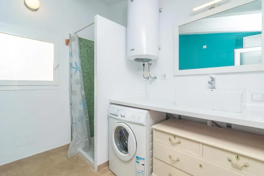 A bright bathroom with a washing machine beneath the counter and a shower area.