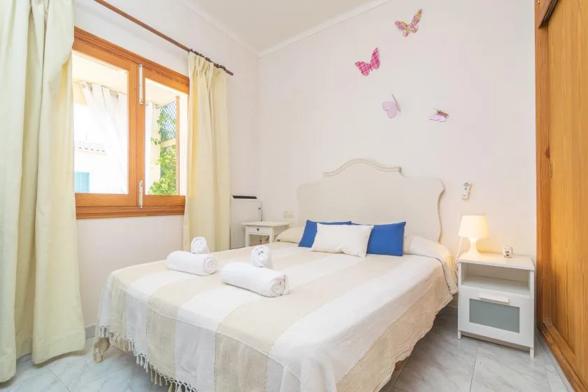 A bright bedroom with a double bed, bedside table, and window.
