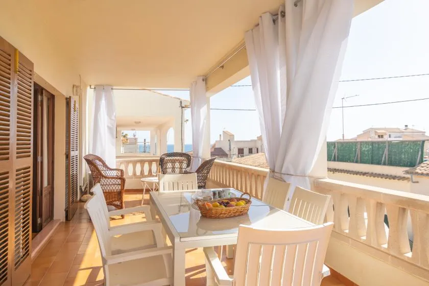 A bright covered balcony dining area with a table and chairs beside open curtains.
