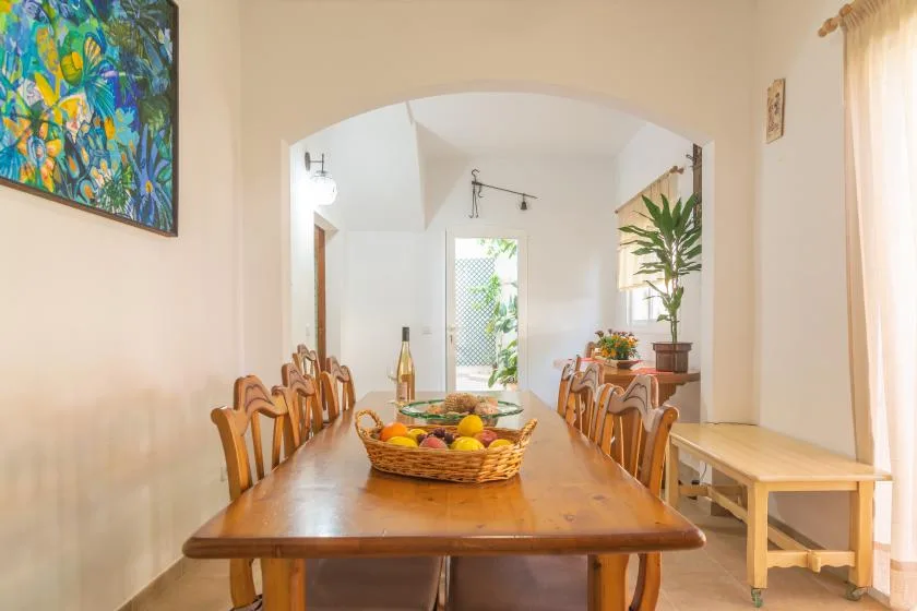 A bright dining room with a long wooden table and a basket of fruit.