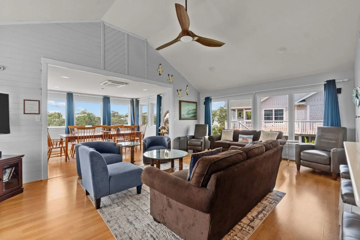 A spacious living room with seating arranged around a coffee table and large windows.