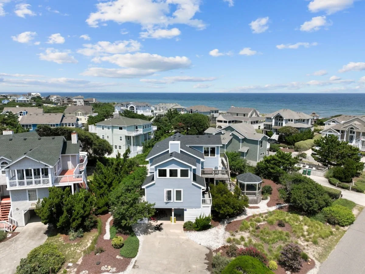 Aerial view of coastal houses among greenery beside the ocean.