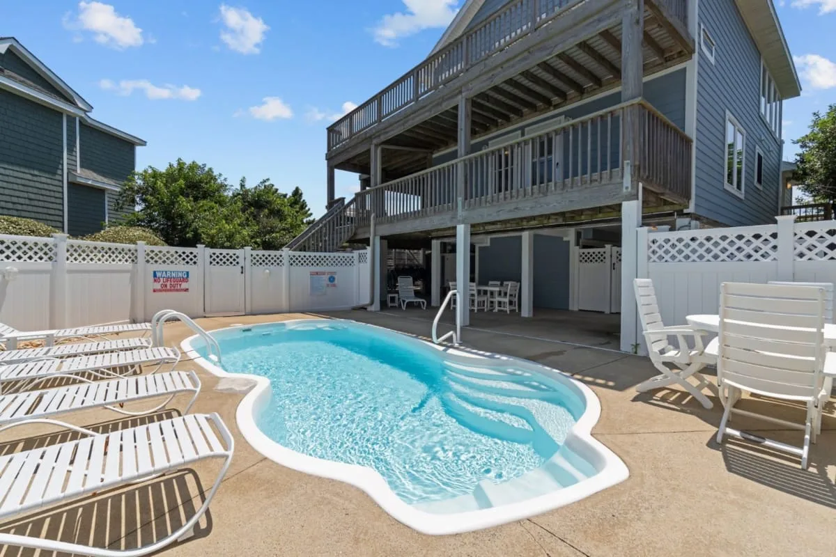 An outdoor swimming pool sits beside a raised deck and patio seating.