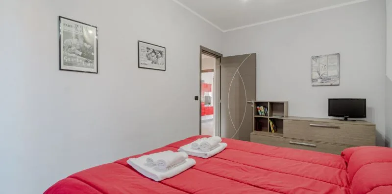 Un dormitorio con una cama roja, toallas dobladas y un mueble bajo.